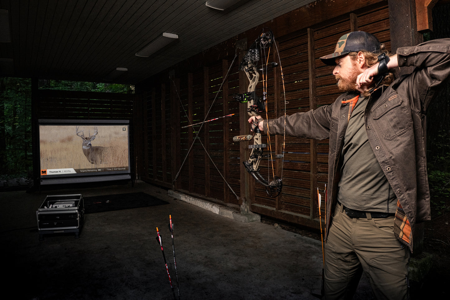 Man practicing archery in a room with a deer on a screen