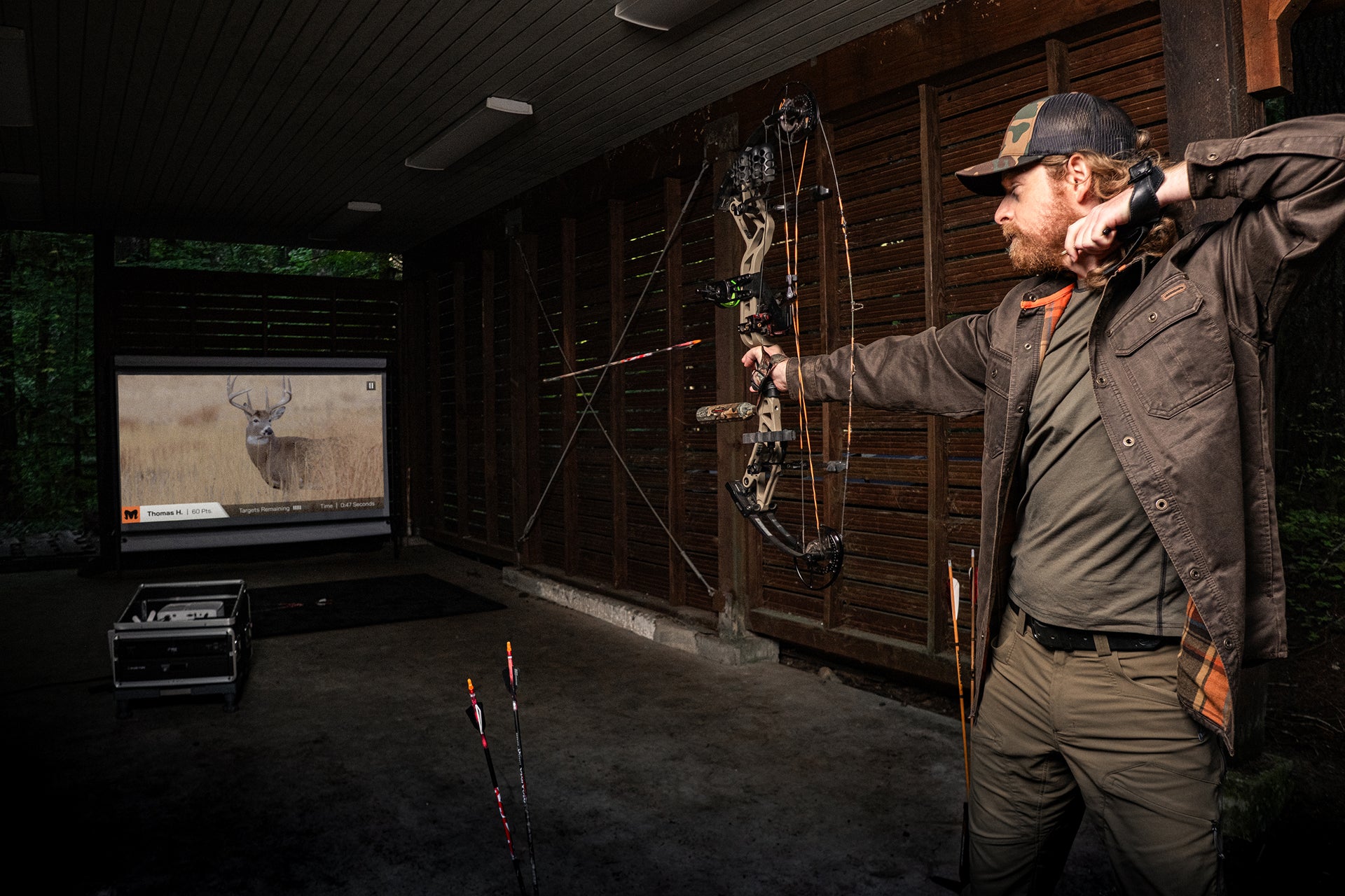 Man practicing archery in a room with a deer on a screen